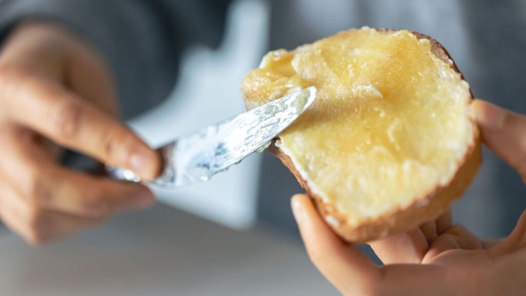 Pessoa espalhando manteiga em uma fatia de pão com uma faca.