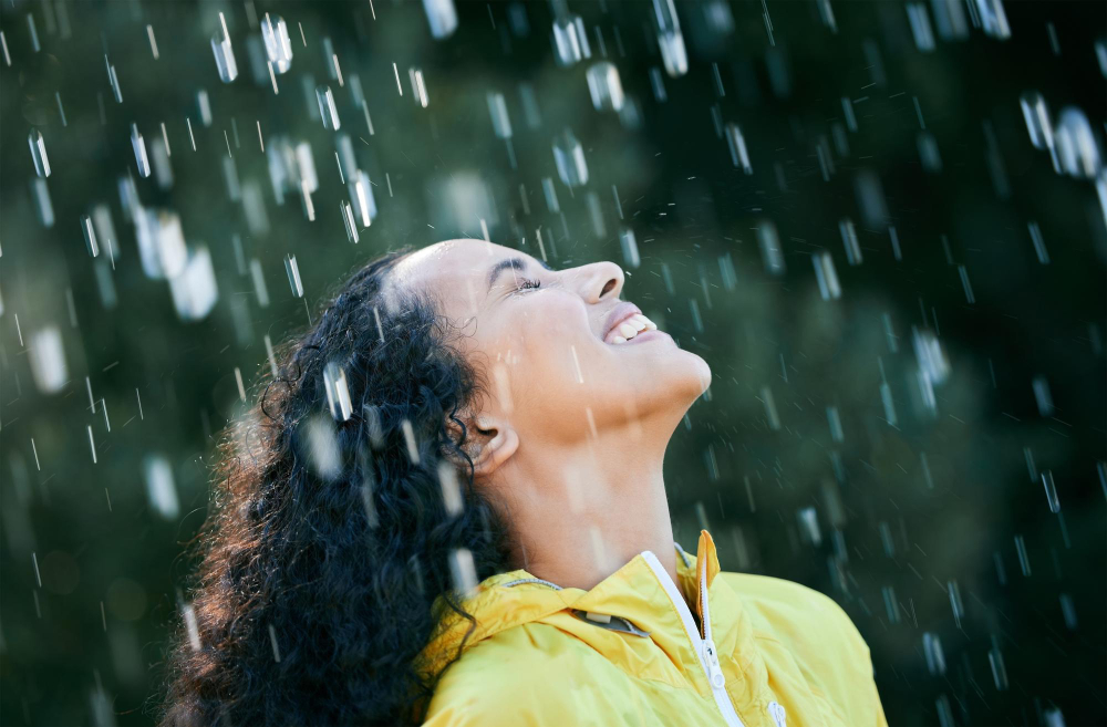 Mulher sorrindo sob a chuva com um casaco amarelo.