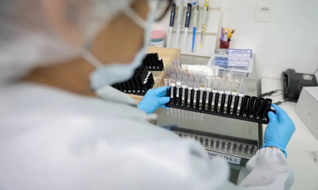 Pessoa em luvas azuis manuseando tubos de ensaio em laboratório.