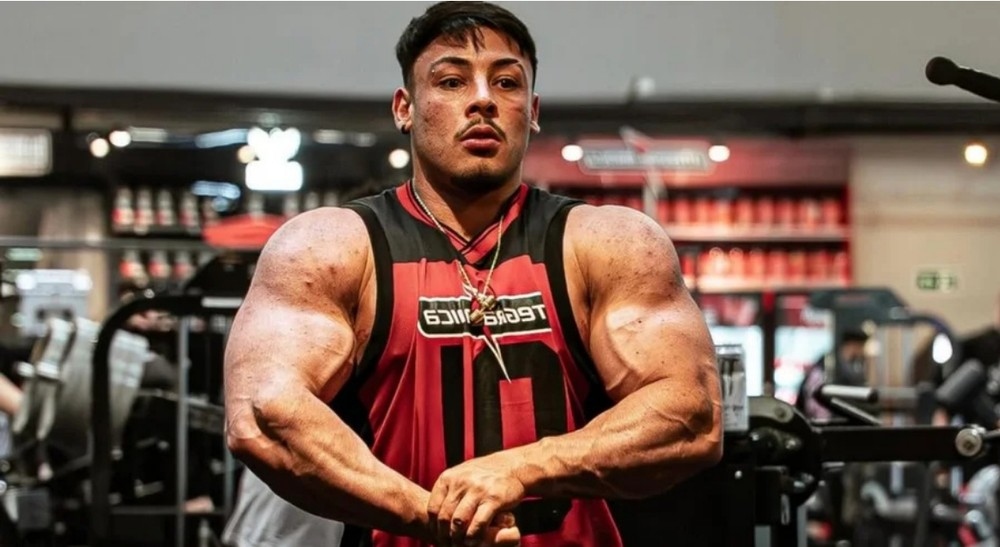 Homem musculoso em pose de fisiculturista na academia.