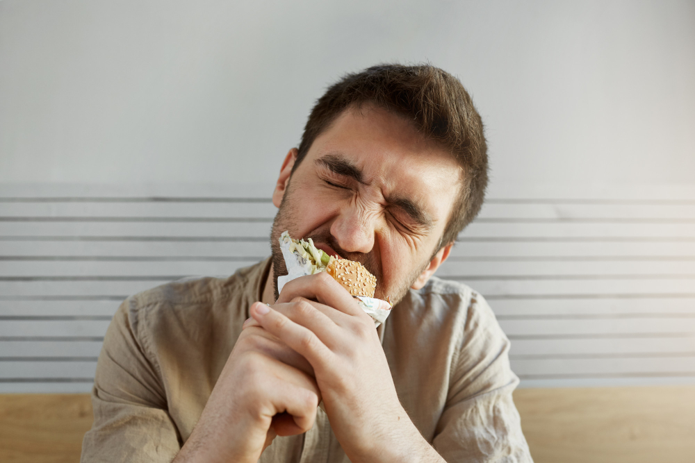 Homem mordendo um sanduíche com expressão intensa de prazer.