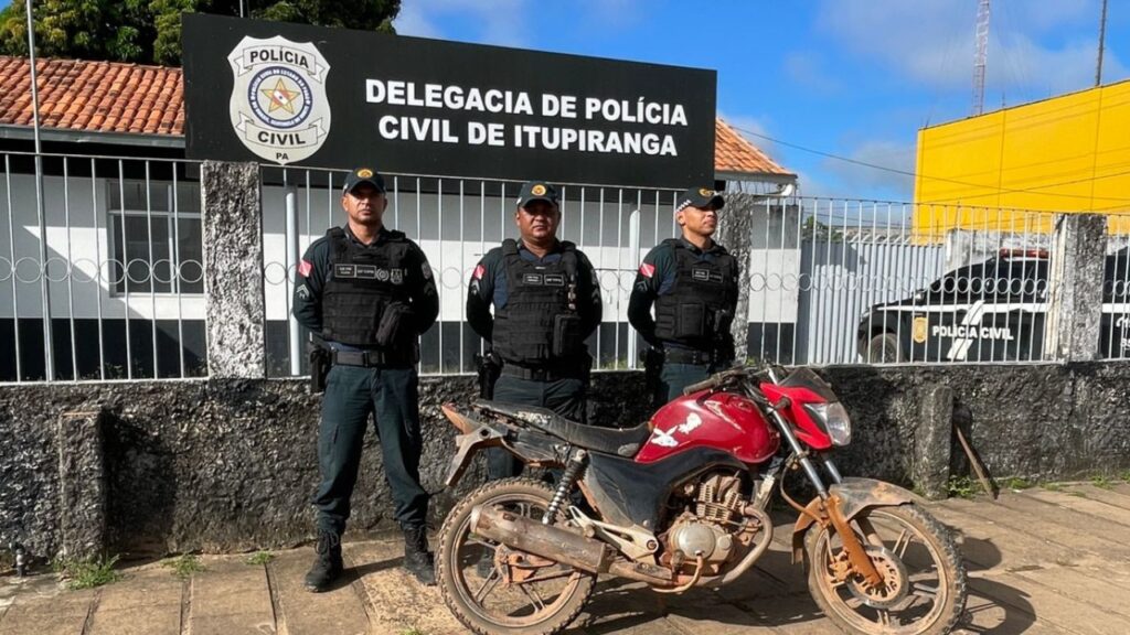 Três policiais civis e motocicleta vermelha recuperada em frente à Delegacia de Itupiranga, PA.