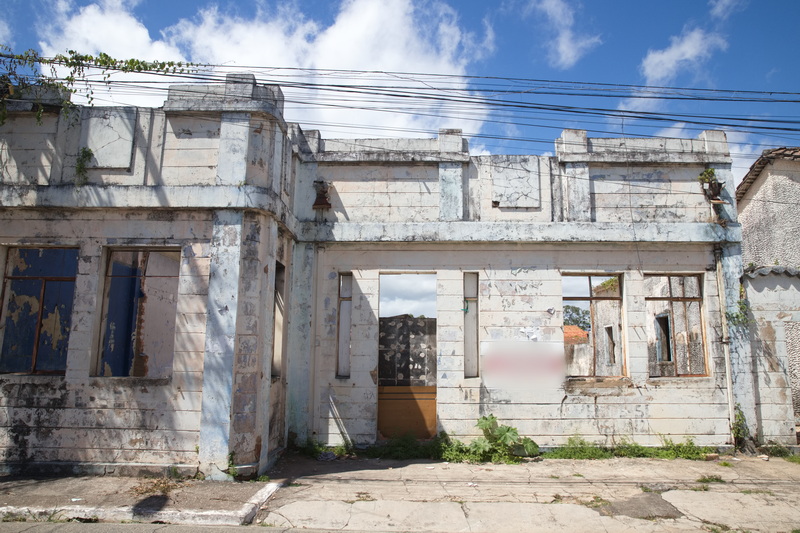 Prédio abandonado com fachada descascada e janelas vazias sob céu azul com nuvens.