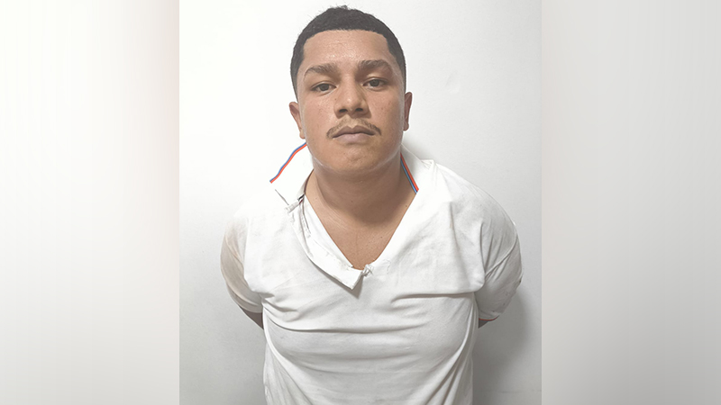 Retrato de um homem com bigode e camiseta branca, olhando para a frente.