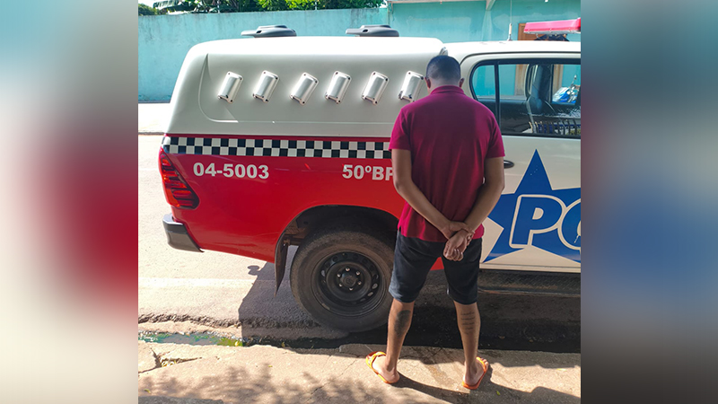 Homem de costas com mãos para trás ao lado de uma viatura policial.