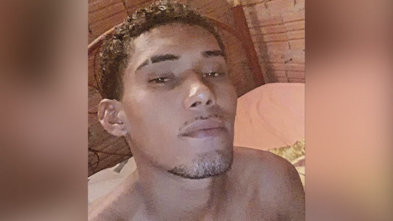 Close-up de um jovem com cabelo cacheado e barba rala, olhando para frente.