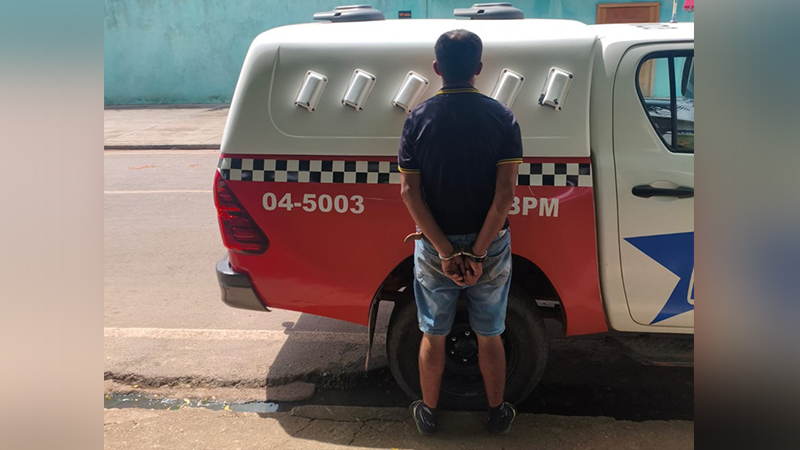 Homem algemado de costas em frente a uma viatura policial.