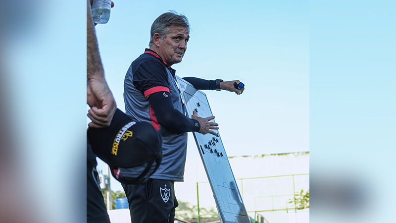 Técnico de futebol explicando táticas em prancheta durante treino.