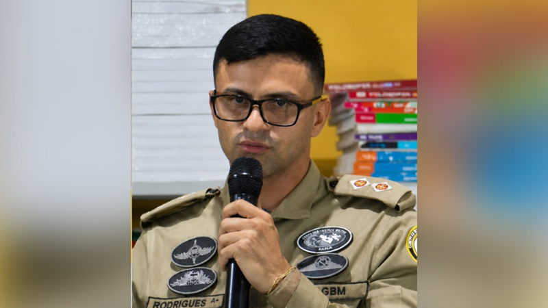 Homem de óculos em uniforme militar segurando um microfone e falando.