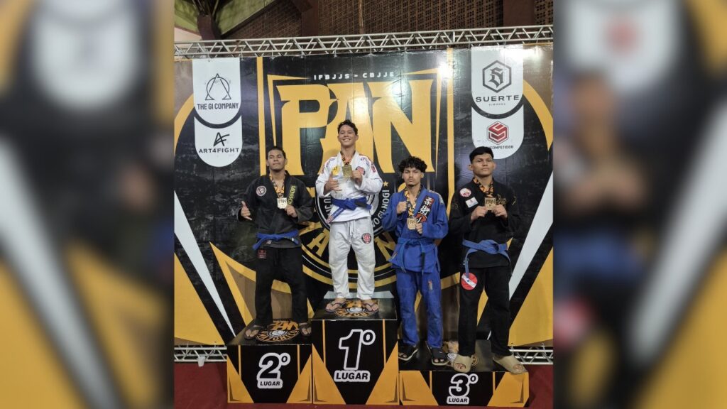 Quatro atletas de jiu-jitsu com suas medalhas em um pódio de competição.