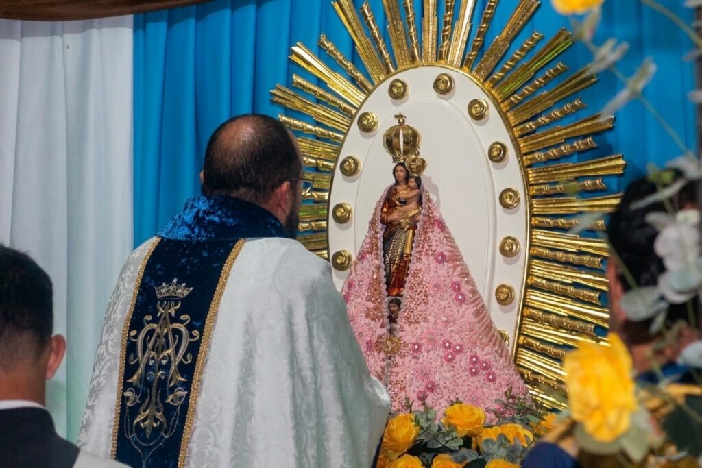 Sacerdote de costas diante de uma imagem religiosa ricamente adornada.
