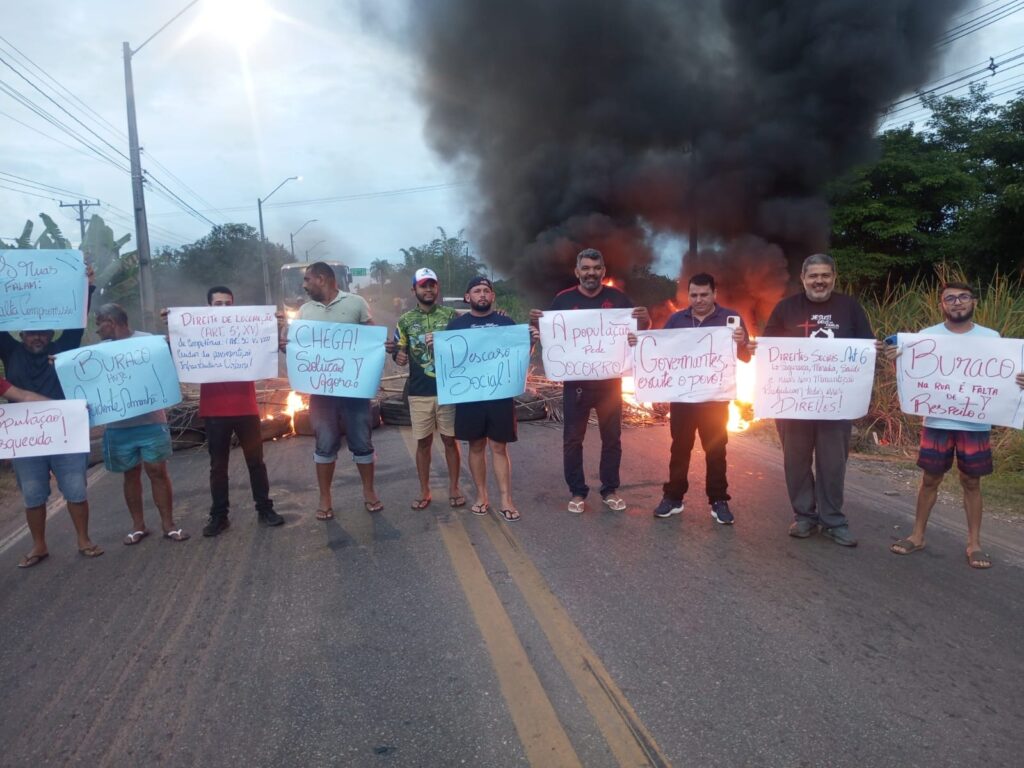 Homens em protesto com cartazes e fogueiras bloqueando estrada.
