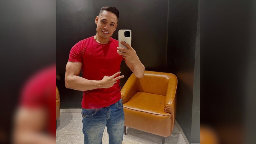 Homem sorrindo fazendo selfie com camiseta vermelha e jeans.