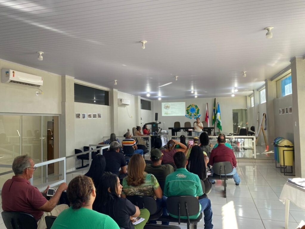Pessoas assistindo a uma palestra em um auditório com projetor e bandeiras.