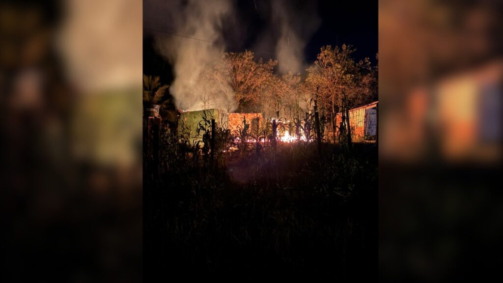 Incêndio noturno em construções rurais com fumaça intensa.