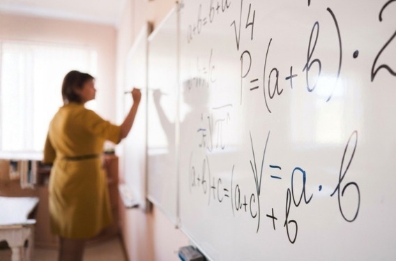 Mulher escrevendo fórmulas matemáticas em um quadro branco.