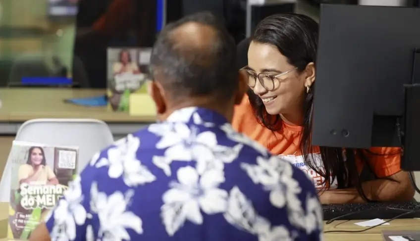 Mulher sorrindo ajudando homem em balcão de atendimento.
