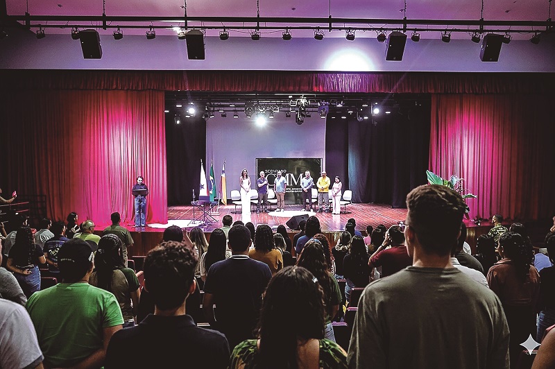 Platéia de um auditório lotado observando um painel de palestrantes em um palco.