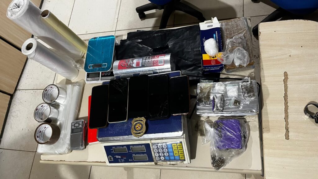 Objetos apreendidos em operação policial, incluindo drogas, celulares e balanças de precisão.
