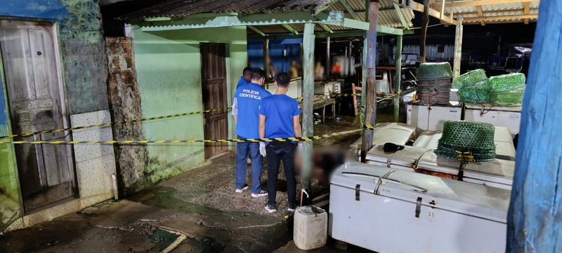 Cena noturna com peritos da Polícia Científica investigando, fita de isolamento, um corpo no chão, freezers e cestos.