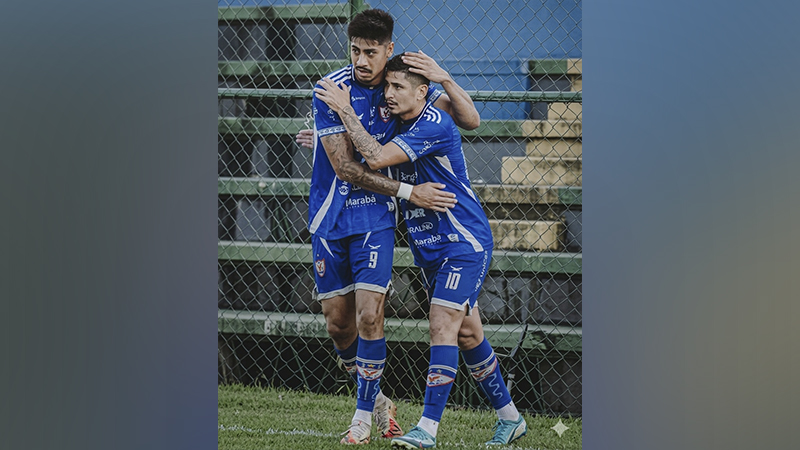 Dois jogadores de futebol com camisas azuis se abraçando no campo.
