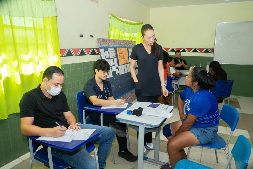 Profissionais de saúde e estudante atendem moradores em ambiente escolar.