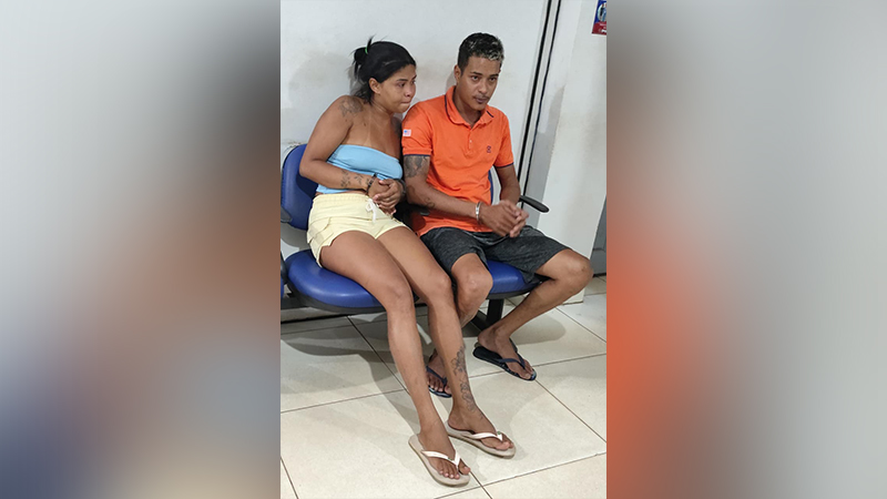Jovem casal sentado em cadeiras azuis em ambiente institucional.
