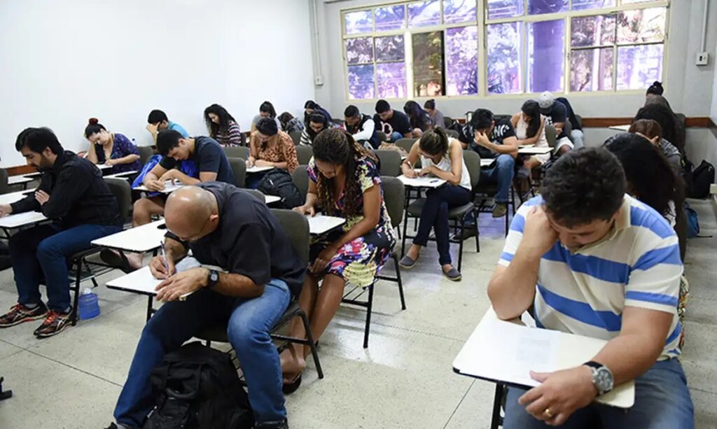 Alunos de diversas idades concentrados em uma prova ou atividade em sala de aula.