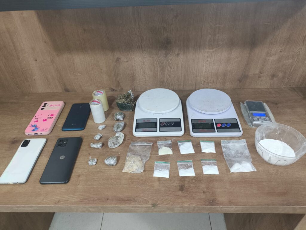 Mesa de madeira com itens apreendidos: dois celulares, duas balanças de precisão, diversas embalagens de drogas (pó e pedras) e maconha.