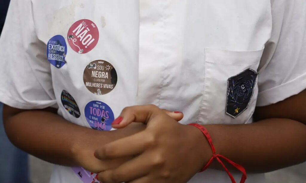 Close-up de uma pessoa com adesivos feministas e de mulheres negras em uma camisa branca.