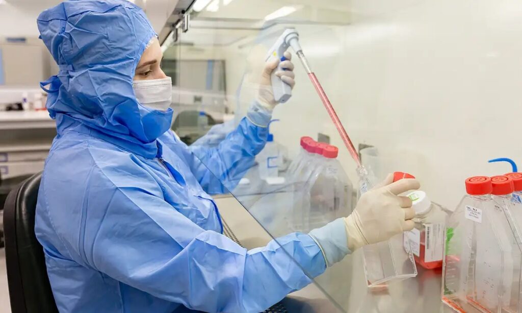 Cientista em laboratório estéril manipulando líquidos com pipeta.