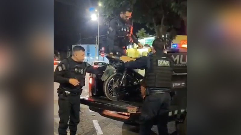 Policiais da ROMU carregando uma motocicleta preta na caçamba de uma caminhonete à noite.