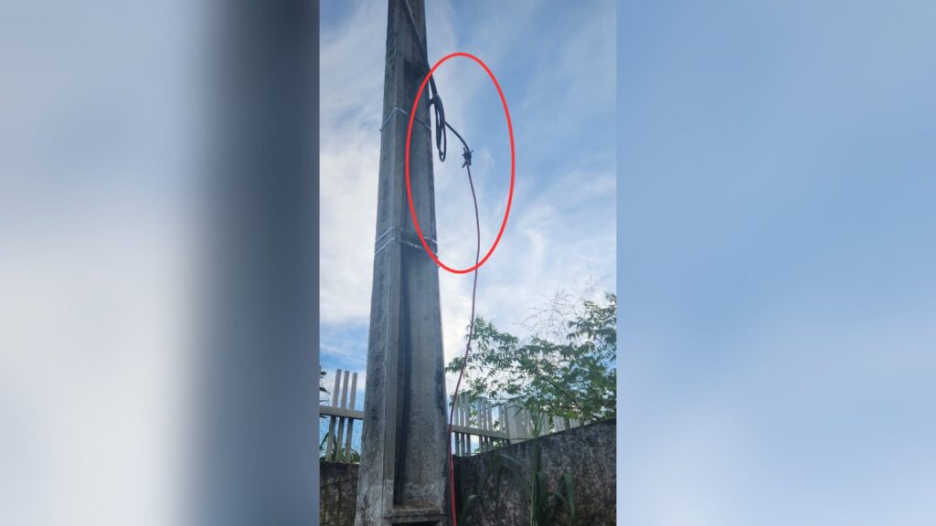Fiação elétrica irregular em poste de concreto, destacada por um círculo vermelho.