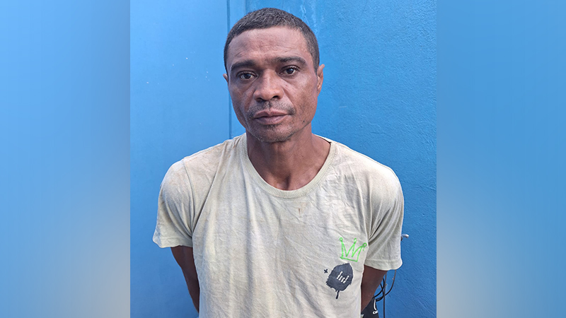 Homem de meia-idade, pele escura, camiseta clara, olhando para frente em fundo azul.