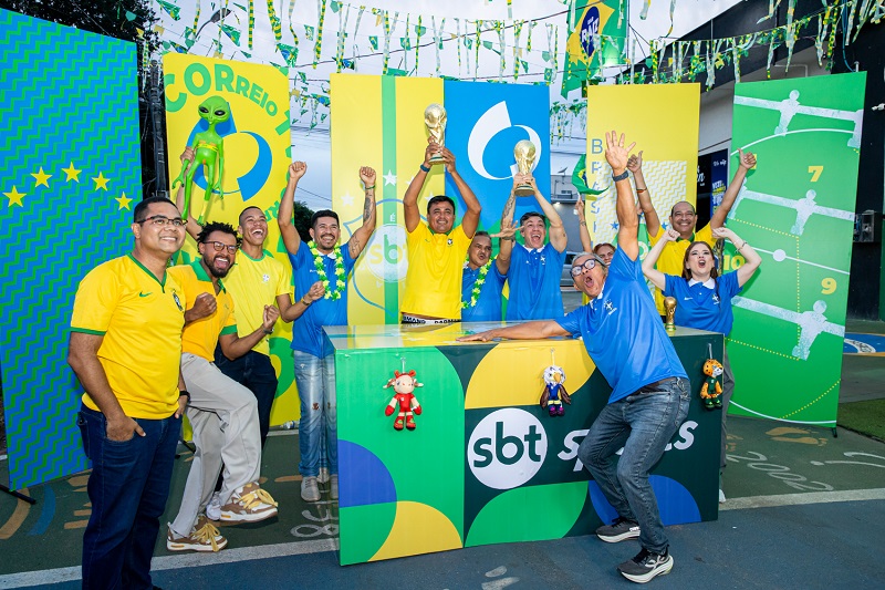 Grupo de pessoas celebrando com alegria em evento de futebol com temática brasileira, troféus e logos "SBT Sports".