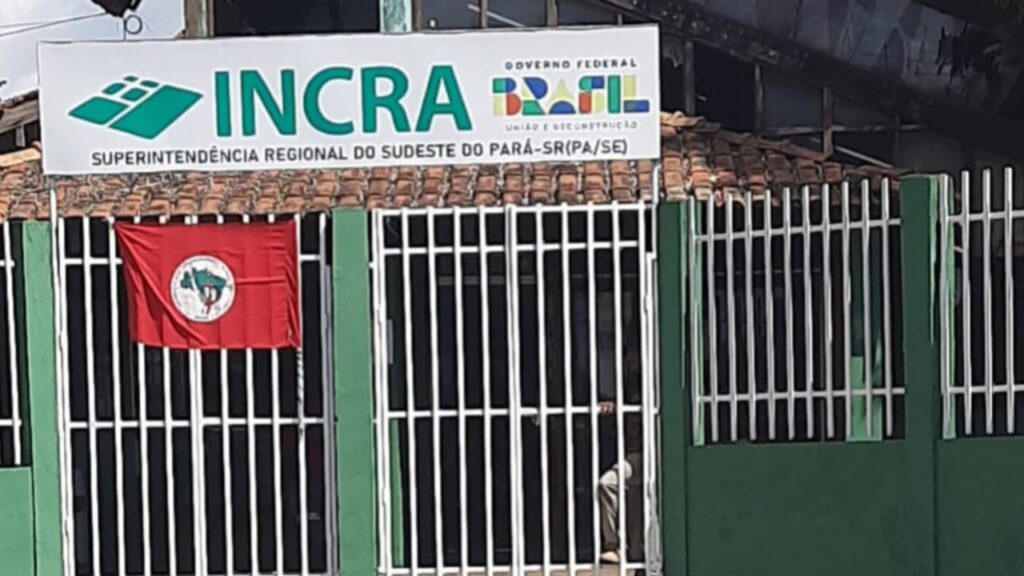 Faixa com logo do INCRA e Governo Federal Brasil, em uma fachada verde com grades brancas.
