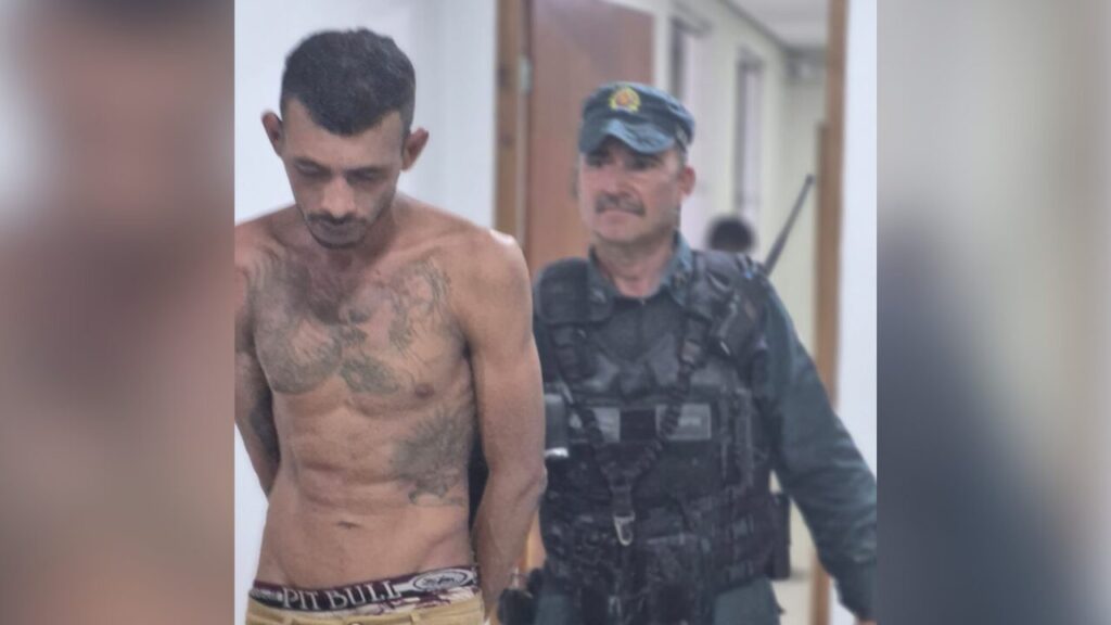 Homem sem camisa algemado sendo conduzido por um policial militar.