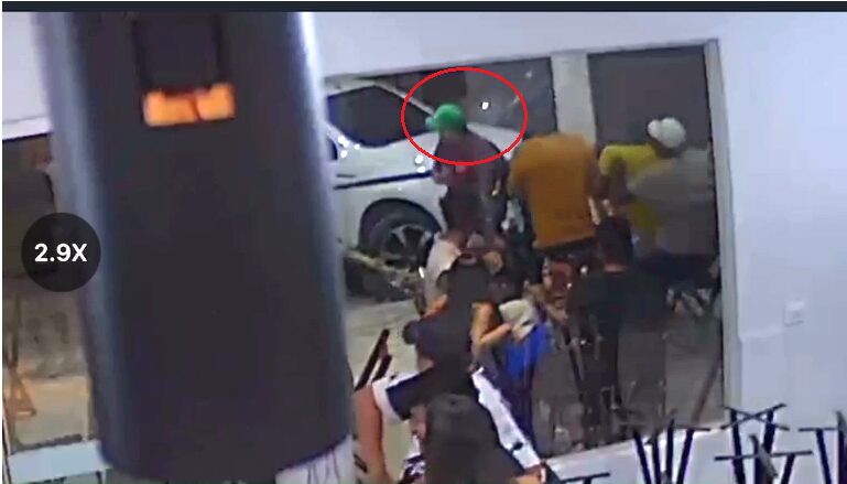 Grupo de pessoas em ambiente interno com carro branco ao fundo.