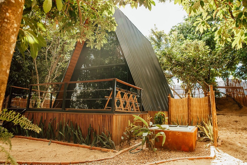 Cabana A-frame moderna com fachada de vidro e deck, cercada por natureza exuberante.