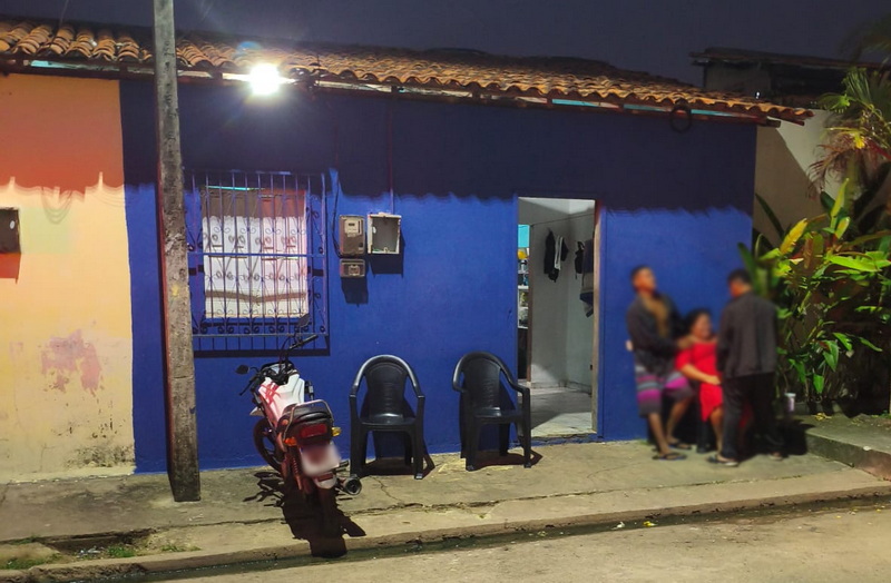 Casa azul vibrante com pessoas e motocicleta estacionada à noite.