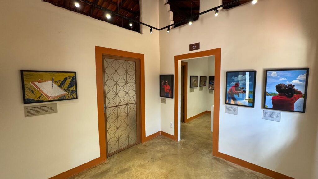 Interior de uma galeria de arte com paredes brancas, molduras laranjas e quadros expostos.