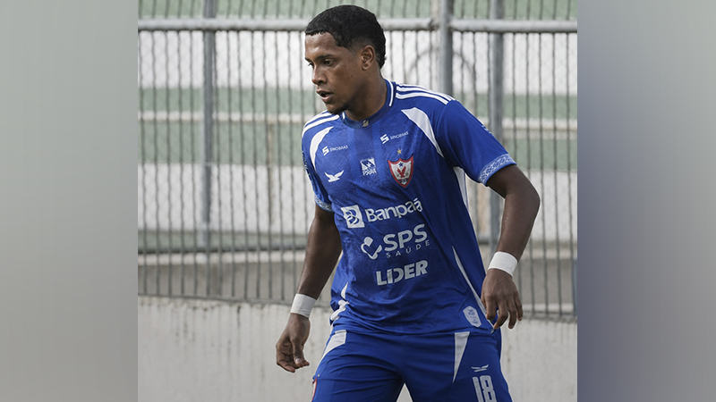 Jogador de futebol em campo, vestindo uniforme azul e branco, com o número 18 visível.
