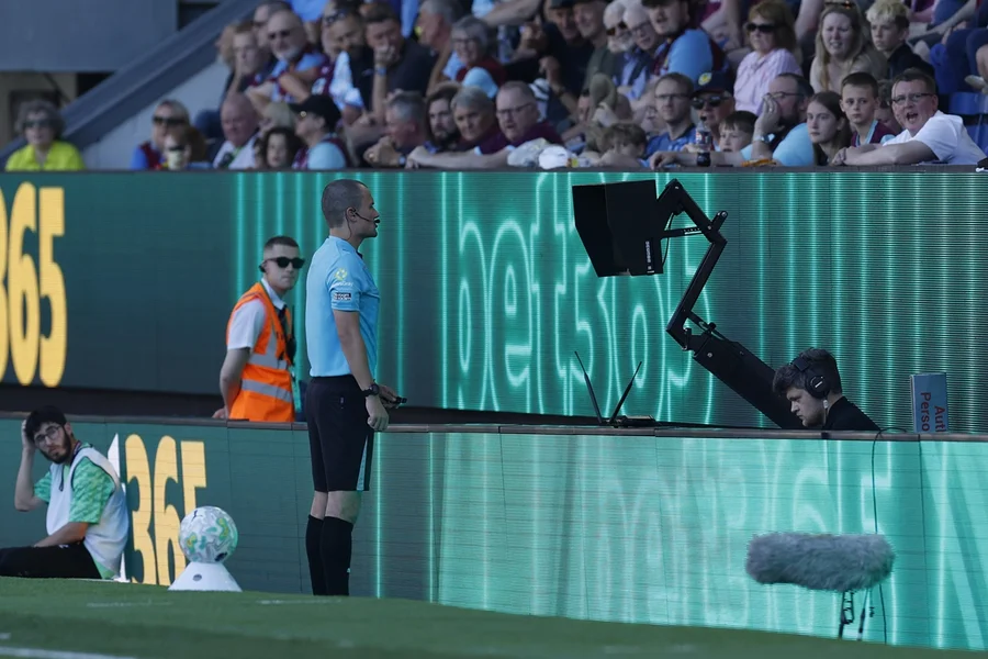 Árbitro de futebol revisando um lance no monitor do VAR à beira do campo