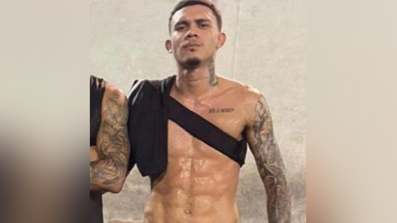 Homem tatuado com o torso nu e faixa preta sobre o ombro.