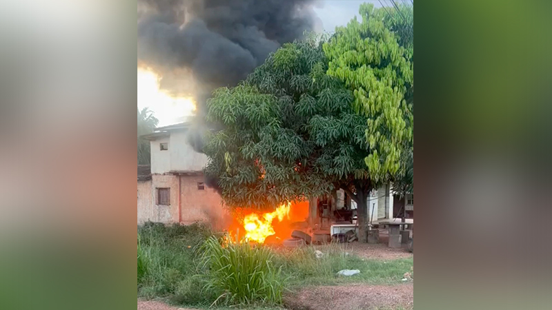 Incêndio com chamas intensas e fumaça preta perto de uma casa e árvores.