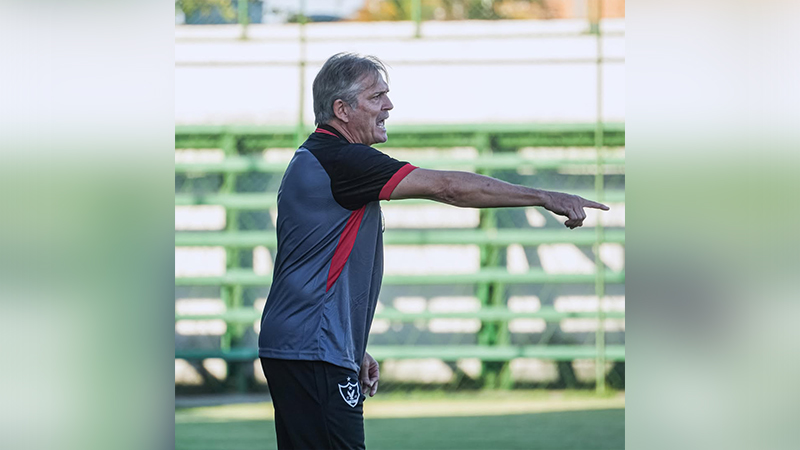 Técnico de futebol masculino com camisa esportiva gesticulando no campo.