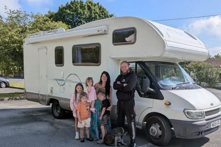 Família posando em frente a um motorhome branco em um estacionamento durante o dia.