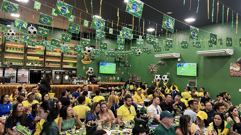 Bar decorado para a Copa do Mundo com bandeiras do Brasil e torcedores vestindo camisas amarelas