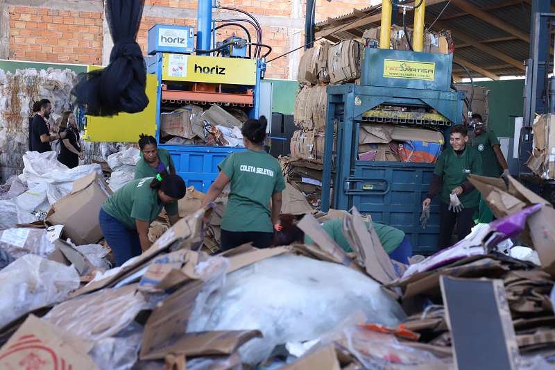Trabalhadores uniformizados operando prensas hidráulicas para reciclagem de papelão em uma cooperativa