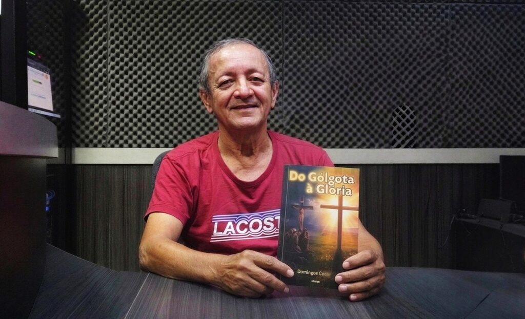 Homem de meia-idade sorrindo, segurando um livro intitulado Do Gólgota à Glória de Domingos Cedar.
